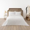 Cuvertura waffle alba 200x220cm asezata pe pat dublu, cu doua fete de perna asortate, in decor luminos si natural