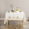 Față de masă Ginny, bumbac 100%, cu iepurași, fluturi aurii și detalii florale pe un fundal pastelat, perfectă pentru decorul de Paște.