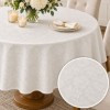 Fata de masa rotunda crem satinata jacquard cu model floral, aranjament cu flori albe si detaliu al tesaturii