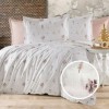 Lenjerie de pat creponata din bumbac 100% cu imprimeu floral delicat in nuante roz-lila, asezata pe un pat matrimonial cu fundal pastel