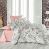 Lenjerie de pat dublu din bumbac 100% creponat, cu imprimeu floral de magnolii roz și frunze gri, prezentată pe fundal cu perete de cărămidă și decor feminin romantic