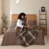 patura Alura Maro First Choice Daily din bumbac si acril cu model in carouri maro crem asezata pe fotoliu
