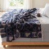 patura Muna Albastra First Choice Daily 200x220 cm cu litere mari bleumarin gri si franjuri decorativi asezata pe fotoliu