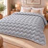 Pilota pufoasa matlasata gri deschis 200x220 cm Ralex Pucioasa, cu model in zigzag si paspoal alb, asezata pe pat matrimonial