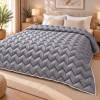 Pilota pufoasa matlasata gri 200x220 cm Ralex Pucioasa, cu model in zigzag si paspoal alb, asezata pe pat matrimonial