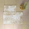 Set de 2 covorașe de baie Tac PasPas Palm bej model frunze tropicale,  plasate pe podea de baie alături de papuci