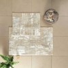 Set de 2 covorașe de baie Tac PasPas în nuanțe de bej, alb si gri, cu design elegant, plasate pe podea de baie alături de papuci