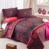 Set de pat cu model oriental în nuanțe de roșu și negru, compus dintr-o cuvertură matlasată de 200x220 cm și două fețe de pernă de 50x70 cm, aranjate într-un decor luminos cu accesorii decorative roșii