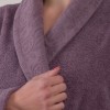 Cuplu purtând halate de baie din bumbac 100%, alb pentru bărbat și mov pentru femeie, lângă prosoape asortate.