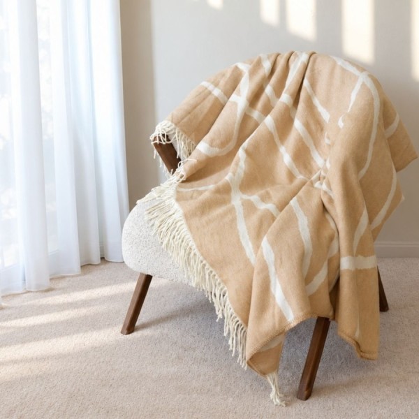 patura Sumina Crem First Choice Daily 200x220 cm cu model geometric crem alb si franjuri decorative asezata pe fotoliu