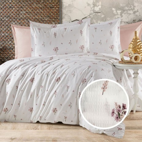 Lenjerie de pat creponata din bumbac 100% cu imprimeu floral delicat in nuante roz-lila, asezata pe un pat matrimonial cu fundal pastel