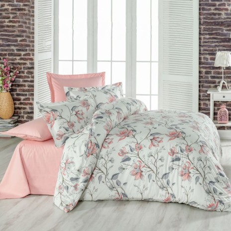 Lenjerie de pat dublu din bumbac 100% creponat, cu imprimeu floral de magnolii roz și frunze gri, prezentată pe fundal cu perete de cărămidă și decor feminin romantic