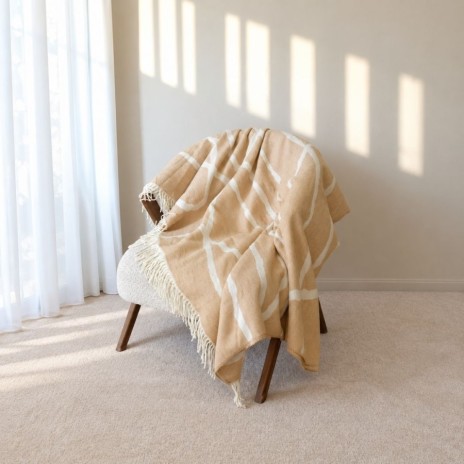 patura Sumina Crem First Choice Daily 200x220 cm cu model geometric crem alb si franjuri decorative asezata pe fotoliu